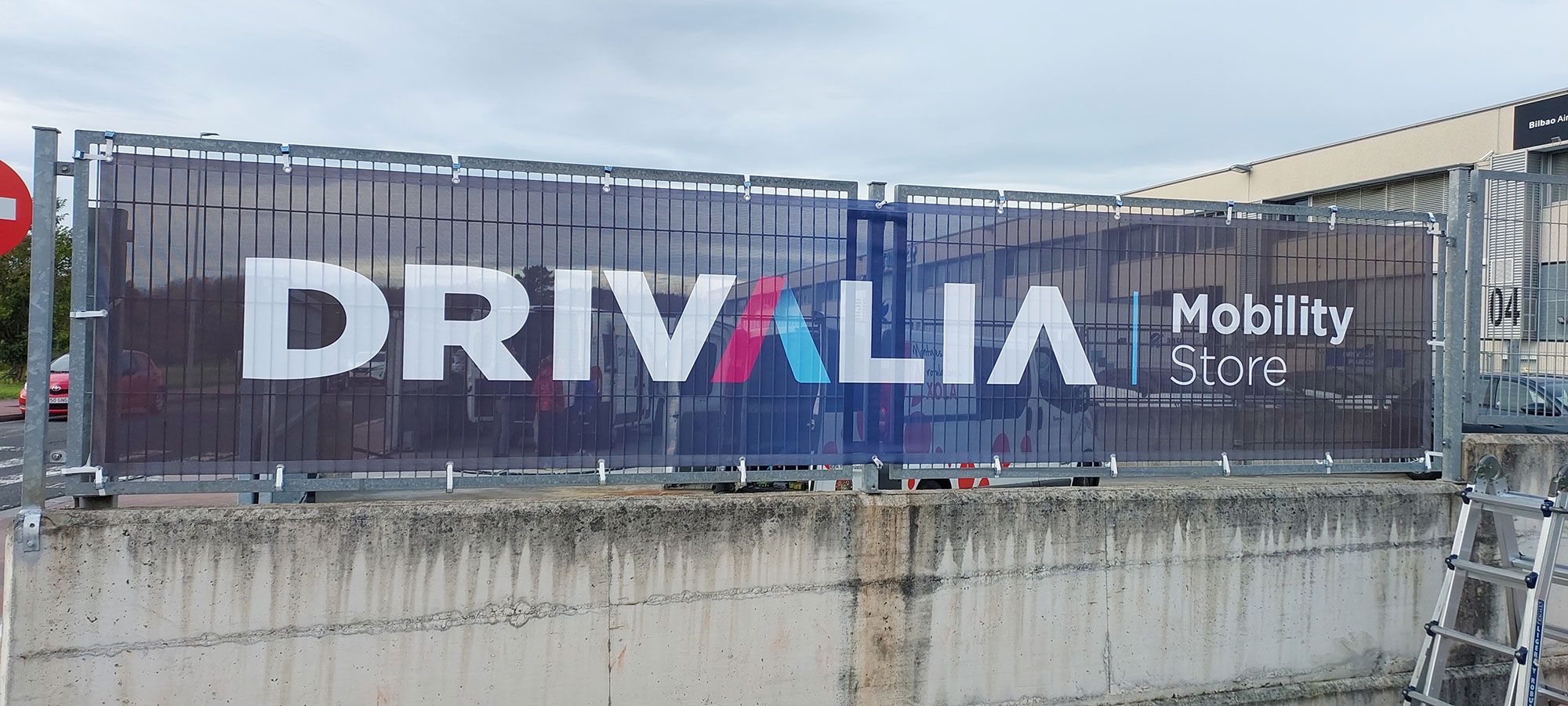 Lona publicitaria Drivalia en valla Lona publicitaria de Drivalia fijada a una valla exterior.